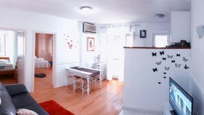 A modern living room with a sofa, dining table, and chairs. There is a TV on a stand, and a wall with butterfly decals. - 3 minutes to the Diocletian's Palace! Two bedroom cosy apartment (Split)