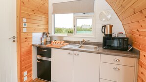 Une petite cuisine aux murs en bois, avec une fenêtre, une horloge et un four à micro-ondes.