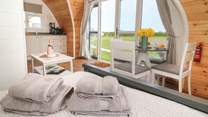Une pièce confortable avec un lit, deux serviettes, une petite table ornée d’un vase de fleurs et une vue sur un paysage verdoyant, visible à travers une grande fenêtre.