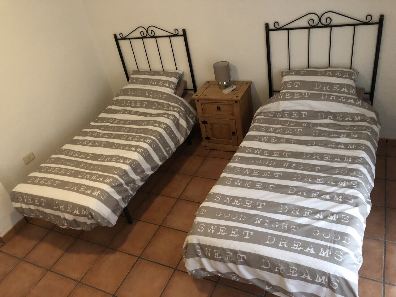 Two single beds with metal frames, each with a wooden nightstand and a bedside lamp.