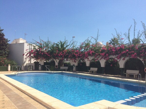 Una piscina con agua azul cristalina, rodeada de un solarium con baldosas.