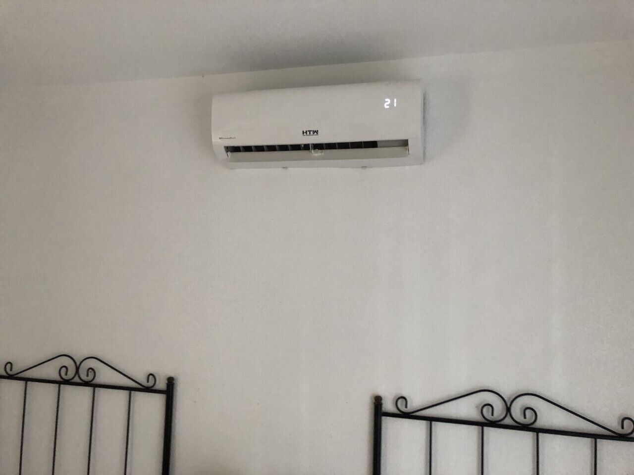 A white air conditioning unit mounted on a plain wall with a metal railing below.