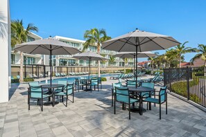 A poolside area with lounge chairs and umbrellas, a pool, and a building with multiple balconies in the background. - ✸NEW✸ 6BR, 500 steps to the beach, Private Pool, Game Room (Melbourne)