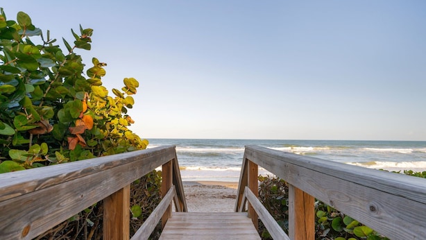 A wooden boardwalk leading to a beach with ocean waves in the background.
