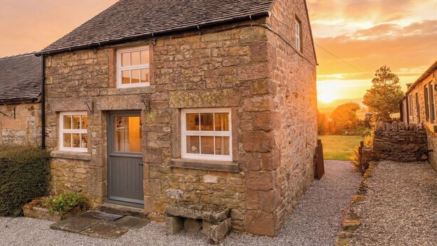 Une maison en pierre avec une porte grise, deux fenêtres et une allée gravillonnée.