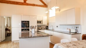Une cuisine moderne avec des meubles blancs, des plans de travail en granit et un îlot central. On y trouve des luminaires suspendus, un four à micro-ondes et un four traditionnel.