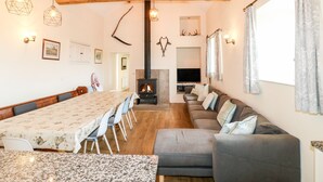 Un vaste salon doté d’un haut plafond en bois, d’une cheminée, d’un coin repas avec une longue table et d’un espace salon confortable.