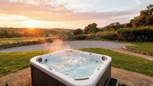 Un bain à remous dans un jardin, avec un mur en pierre et une rivière en arrière-plan.