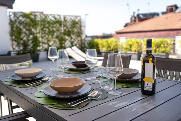 A dining table set with plates, bowls, cutlery, and wine glasses, with a bottle of wine on the right. - San Ferdinando Terrace, Naples (Napoli)