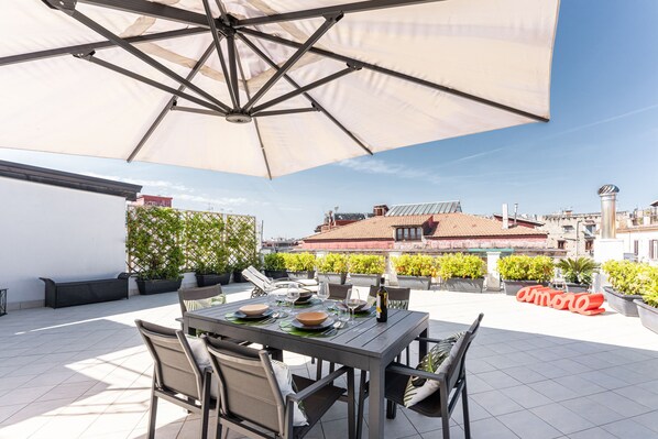 An outdoor patio with a table set for dining, surrounded by chairs and a large umbrella. - San Ferdinando Terrace, Naples (Napoli)