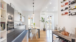 Una cuina moderna amb electrodomèstics integrats, una zona de dinar amb taula i caires, i una prestatgeria de vi a la paret.