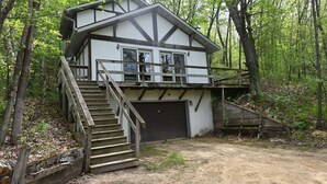 A two-story cabin with a staircase leading to the upper level, surrounded by a forest. - The Incline (Norwalk)