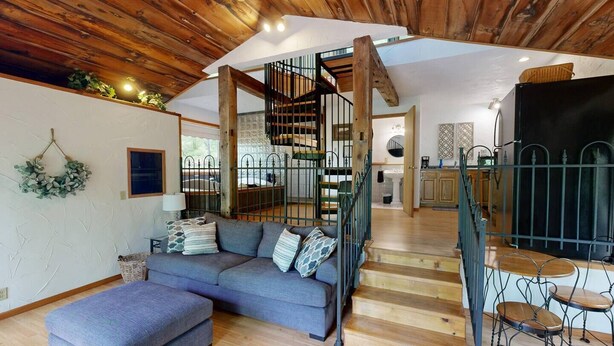 A modern interior with a wooden ceiling, a grey sofa, a staircase, and a kitchen area. - The Incline (Norwalk)