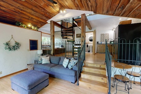 A modern interior with a wooden ceiling, a grey sofa, a staircase, and a kitchen area.. The Incline