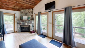 A room with a stone fireplace, a television mounted on the wall, and large sliding glass doors leading to an outdoor area. - The Incline (Norwalk)