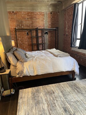 A bed with white bedding in a room with exposed brick walls and a wooden headboard. - Central City Condo (Phoenix)