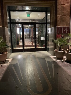 A hotel entrance with a glass door, a visible exit sign, and a number '114' on the wall.
