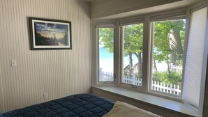A bedroom with a bed, a window with a view of trees and a white fence, and a framed picture on the wall.