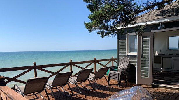 A wooden deck with chairs overlooking the ocean, a small building with a sliding door, and a clear view of the sea.