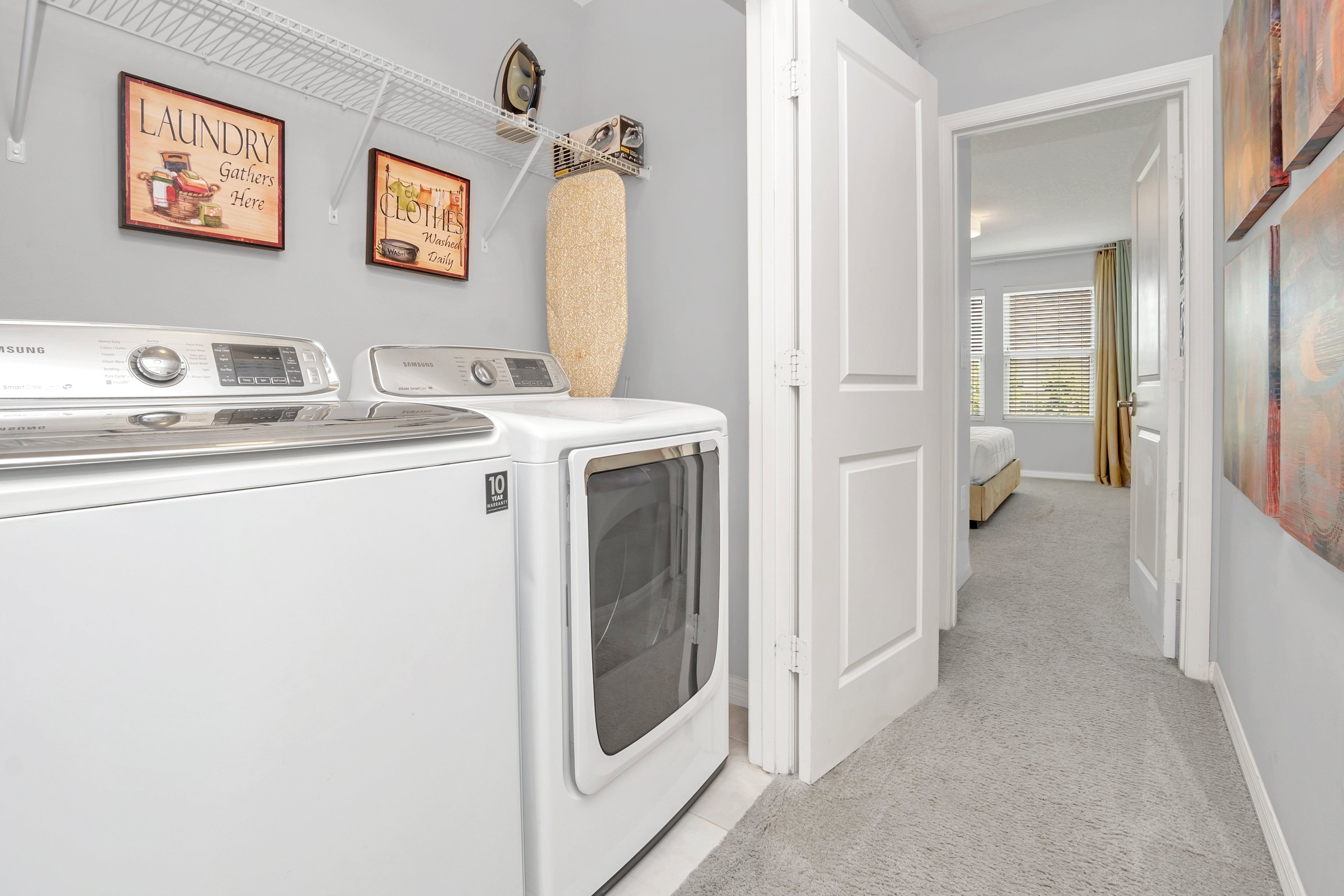 A laundry room with a front-loading washer and dryer, a drying rack, and two wall-mounted drying racks.