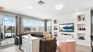 A modern living room with a sofa, a pink ottoman, and a TV mounted on the wall. - EV_3115 - 4 Bed 3.5 Bath Screened-In Splash Pool, Kids Bedroom, Games Room (Kissimmee)
