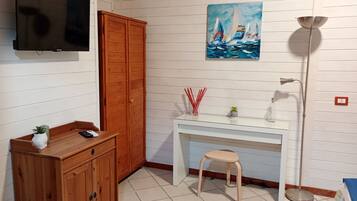 Ein Zimmer mit einem Holzschrank, einem Schreibtisch mit Hocker, einem Segelboot-Gemälde und einer Stehlampe.
