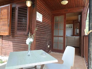 A wooden cabin with a dining area featuring a table and chairs, a vase with flowers, and a kitchen visible through a glass door. - Summer Paradise (Ispani)