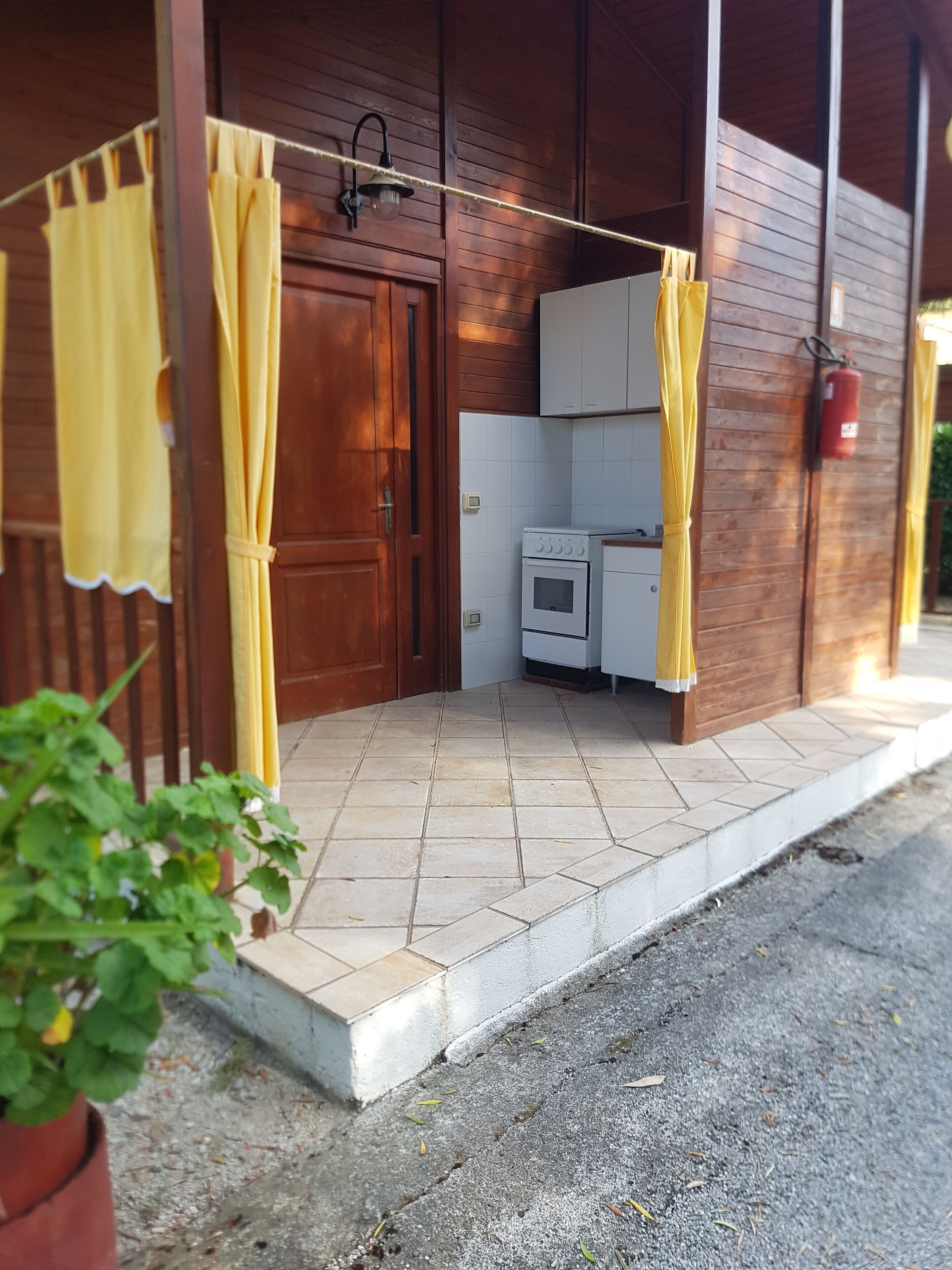 Un bâtiment en bois avec une entrée carrelée, une porte et un petit coin cuisine équipé d’un poêle et de placards.