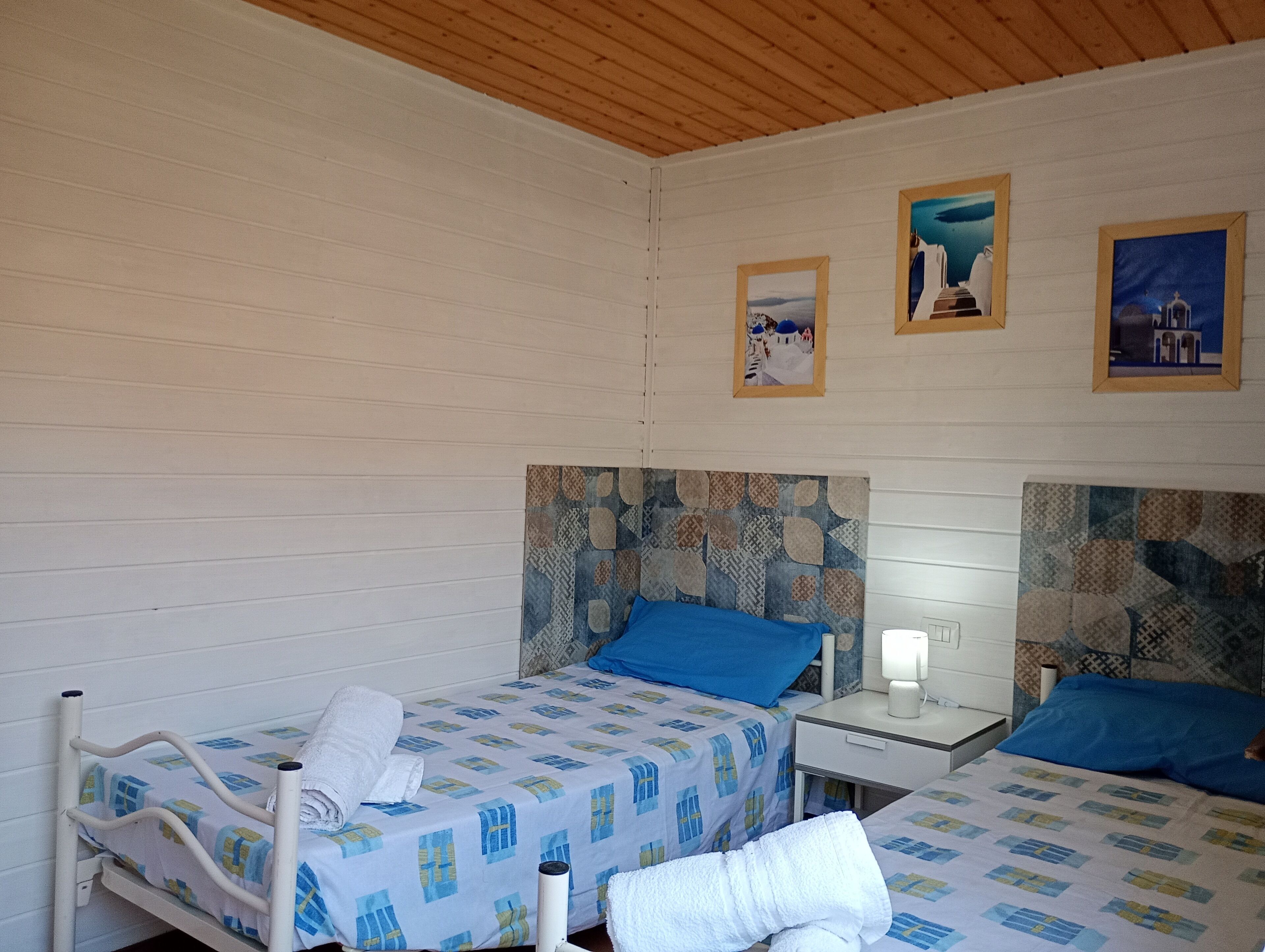 Habitación con dos camas, cada una con una colcha de diseño azul y blanco, cabeceros de madera y una pared blanca decorada con tres cuadros.