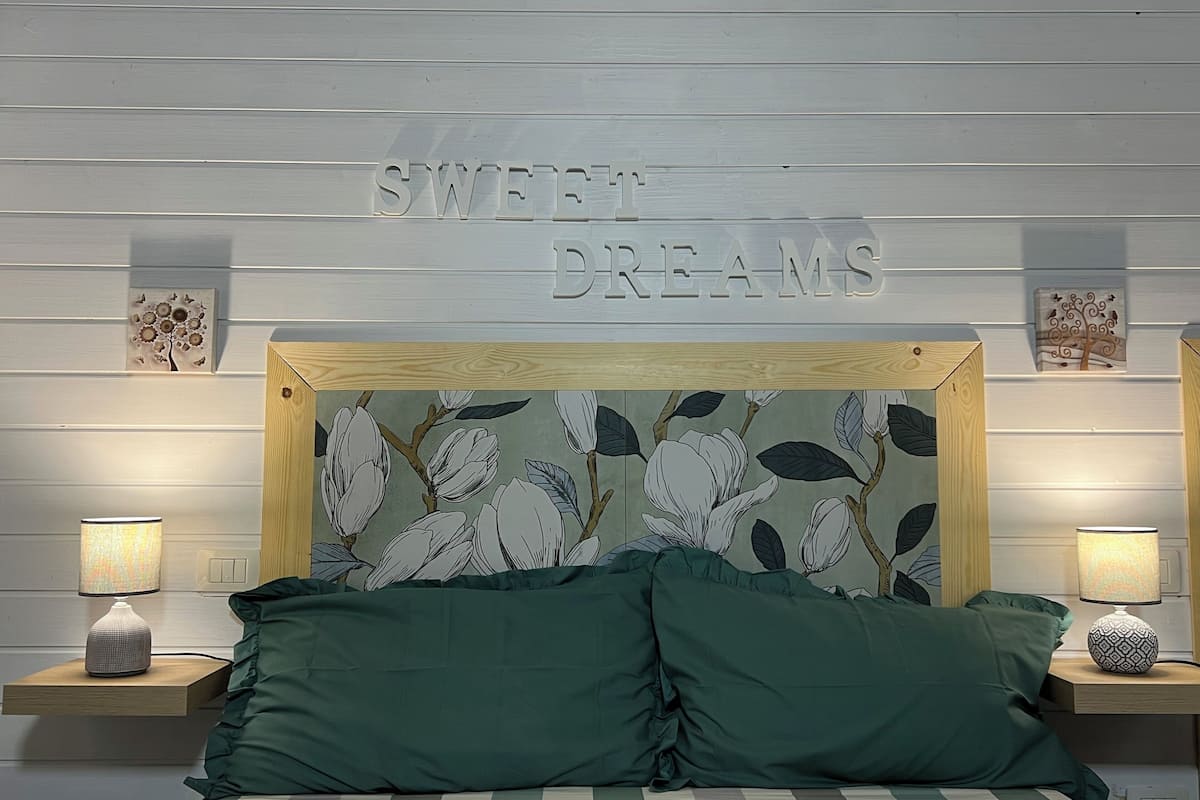 A bed with green pillows, a headboard with a floral pattern, and a wall with the words "SWEET DREAMS" above it.