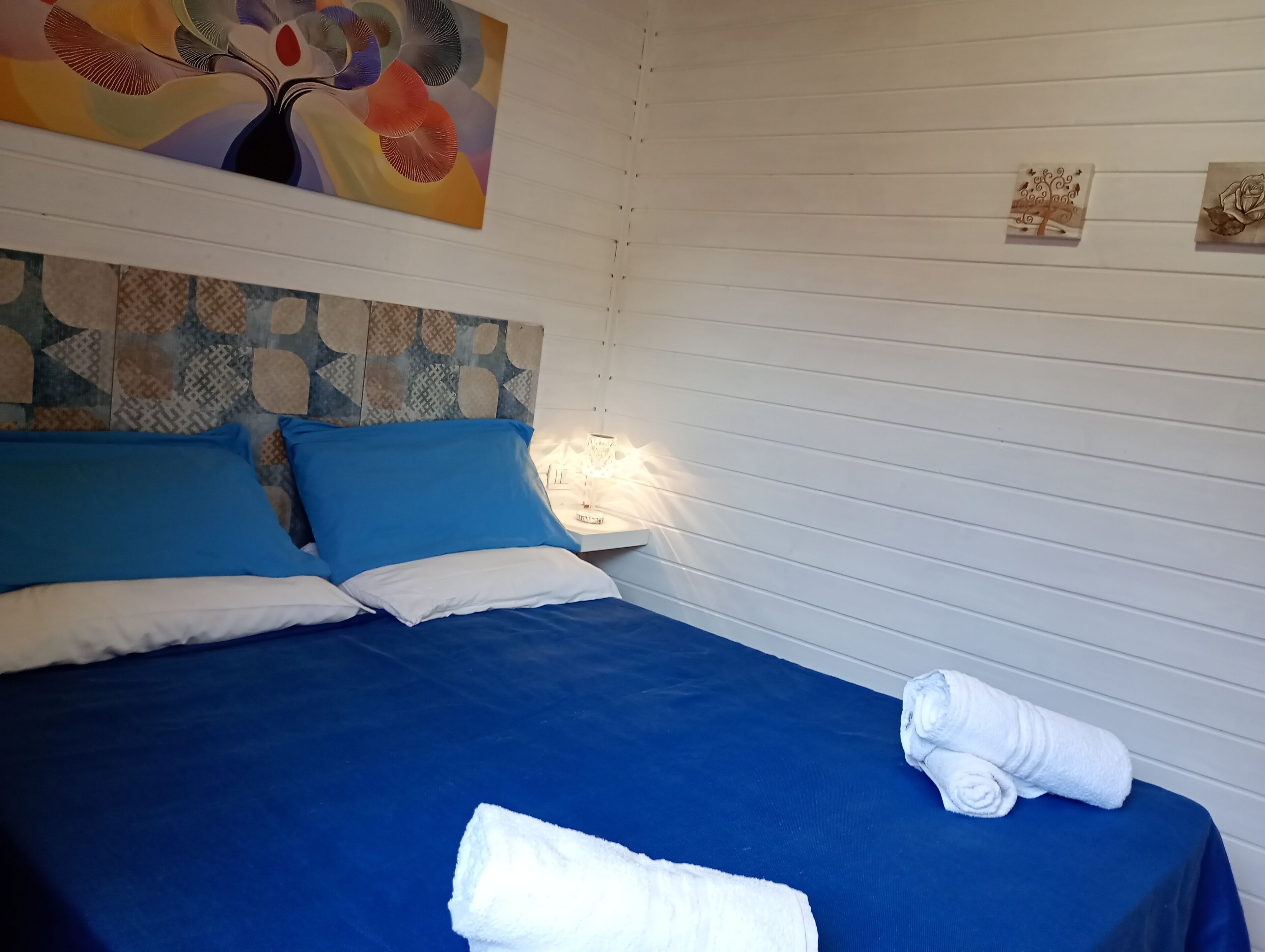Una cama bien hecha con ropa de cama azul y blanca, un cabecero decorativo y una lámpara fijada a la pared.