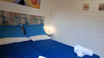 Una cama bien hecha con ropa de cama azul y blanca, un cabecero decorativo y una lámpara fijada a la pared.