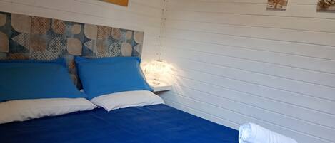 A neatly made bed with blue and white bedding, a decorative headboard, and a wall-mounted lamp.