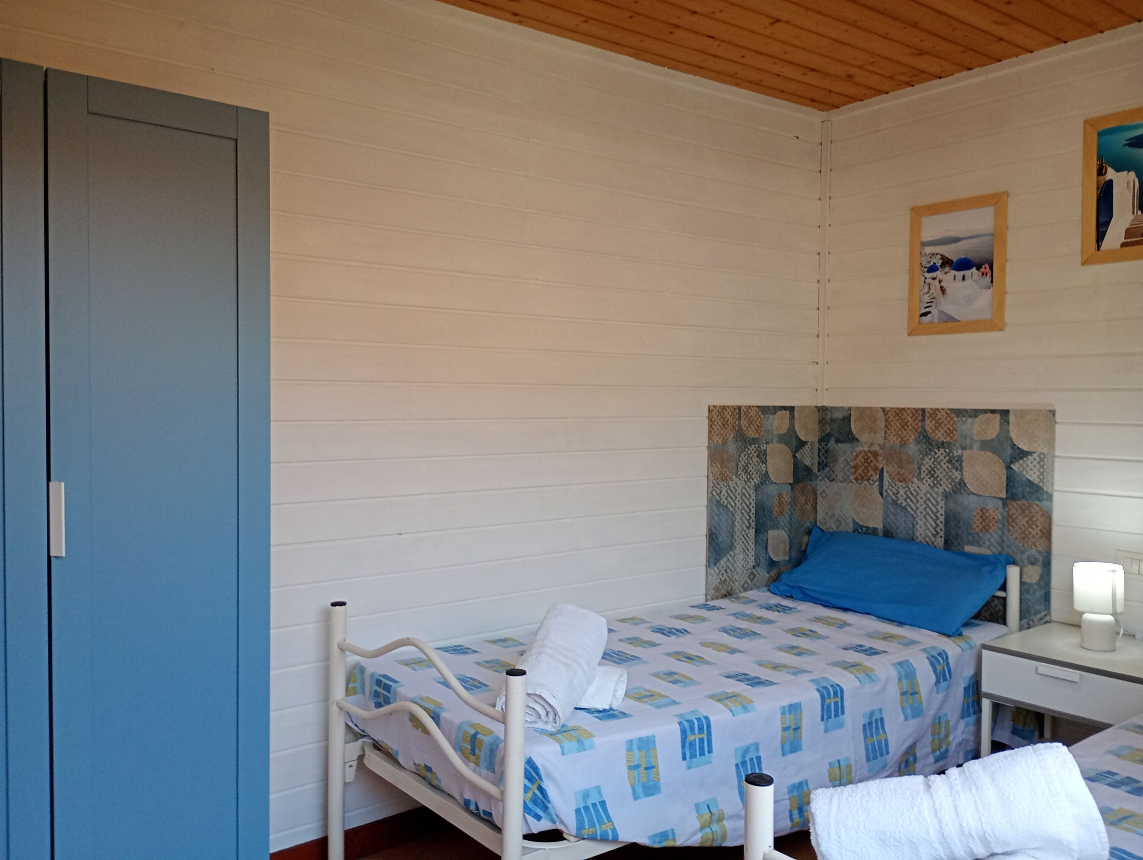 Una habitación con cama, mesita de noche, lámpara, armario y un cuadro en la pared.