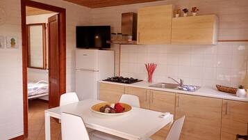 A compact kitchen with a dining area, wooden cabinets, a built-in TV, and a small refrigerator.
