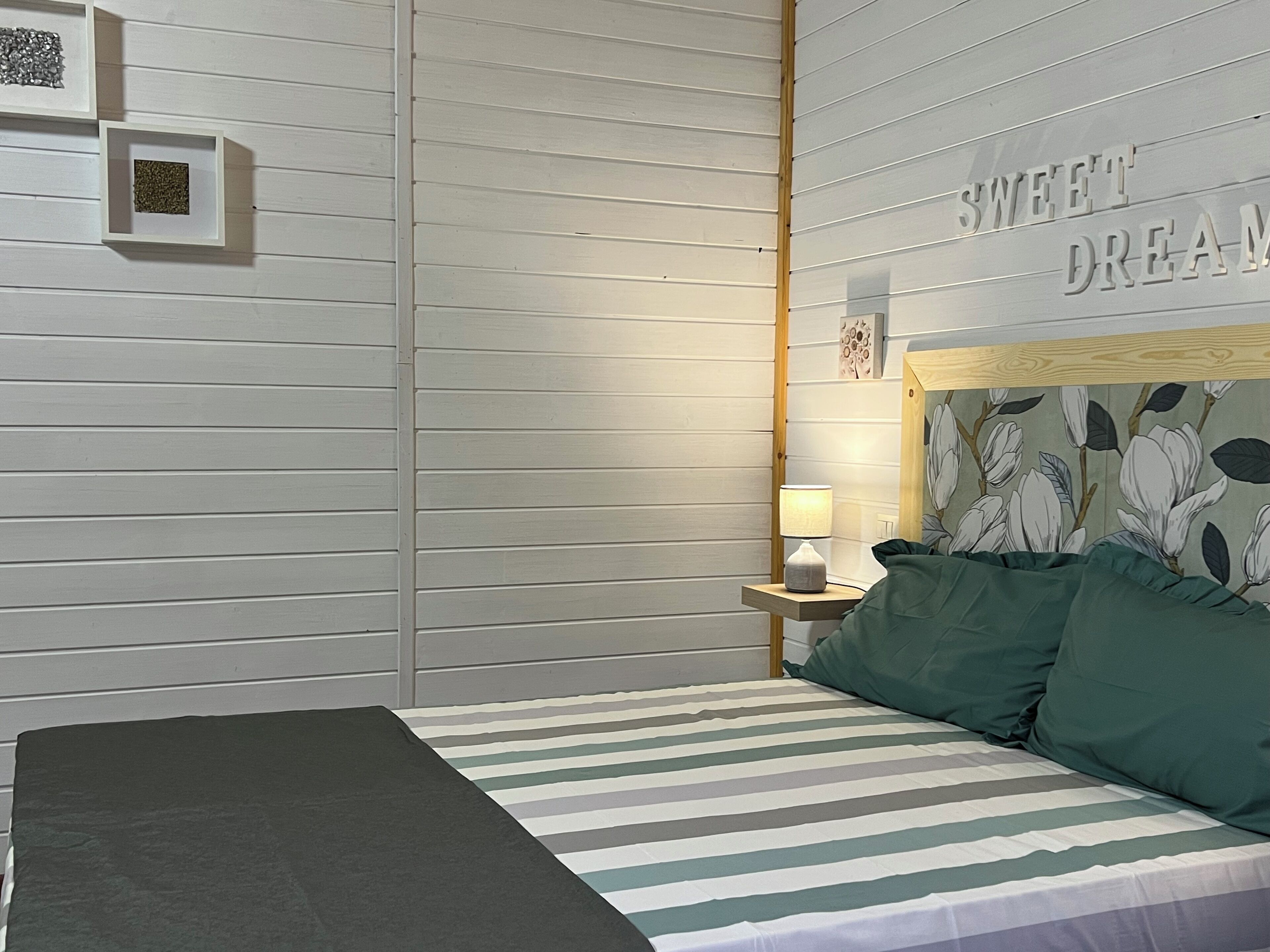 A bedroom with a bed, a nightstand, a lamp, and a wall with a floral pattern and the text "SWEET DREAMS".
