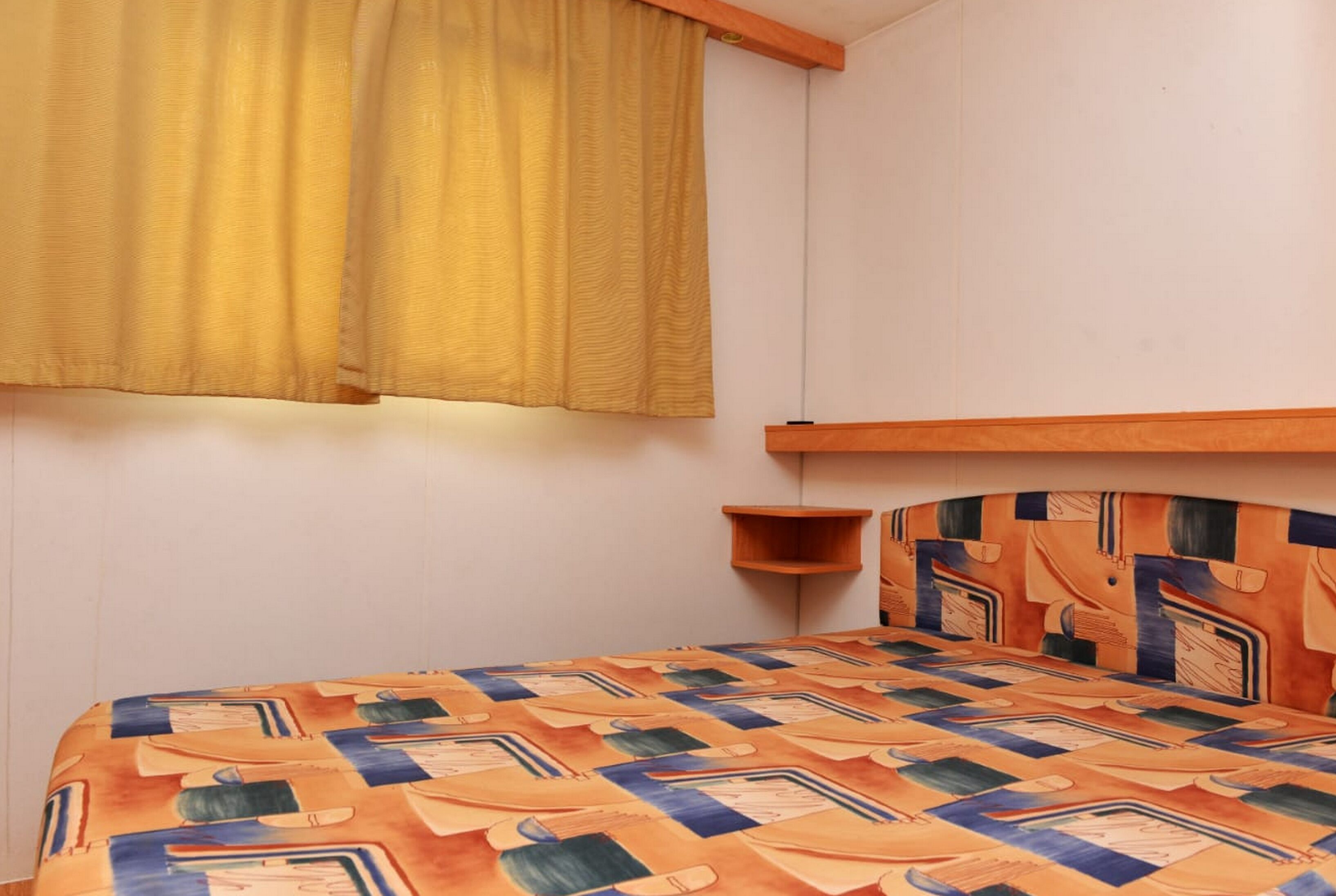 Una habitación con cama, ventana con cortinas amarillas y cabecera con diseño geométrico.