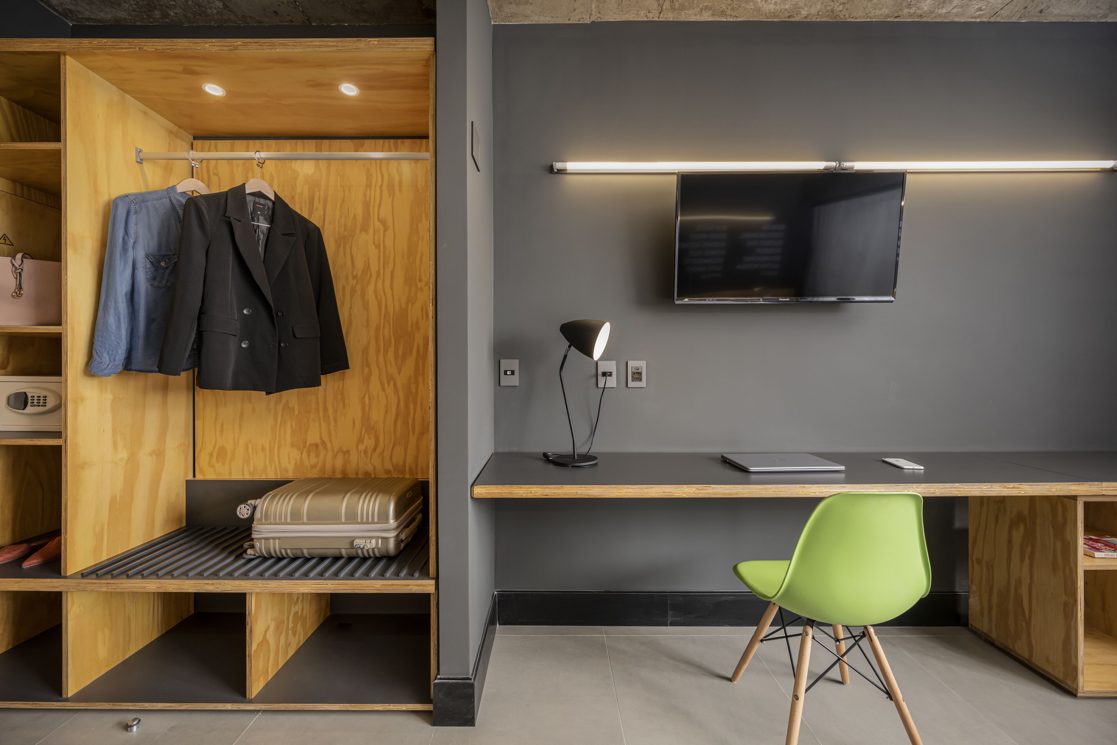 A modern room with a wooden wardrobe, a desk with a laptop, a green chair, and a television.