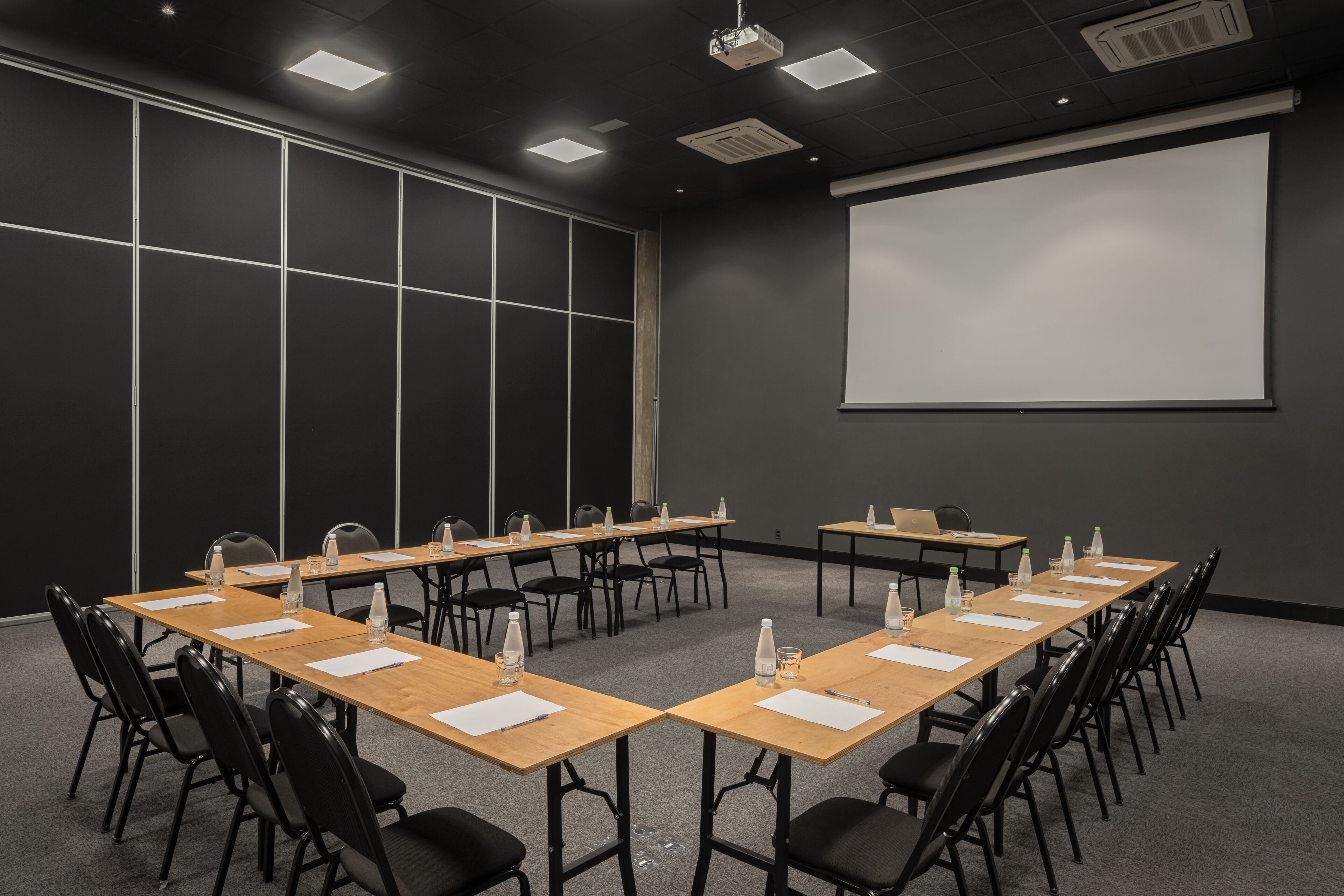 Un salón de conferencias con mesas largas, sillas y una pantalla para proyector.