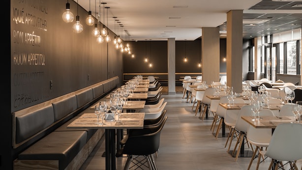 Un restaurante moderno con mesas largas, luces colgantes y un interior oscuro.