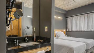 Quarto de hotel moderno com um espelho grande, uma pia, duas camas e teto com vigas aparentes.
