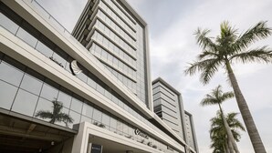 Un edificio moderno de varios pisos con un llamativo letrero de 'Doctor City', que presenta un diseño arquitectónico limpio con ventanas de vidrio reflectante y una palmera en primer plano.