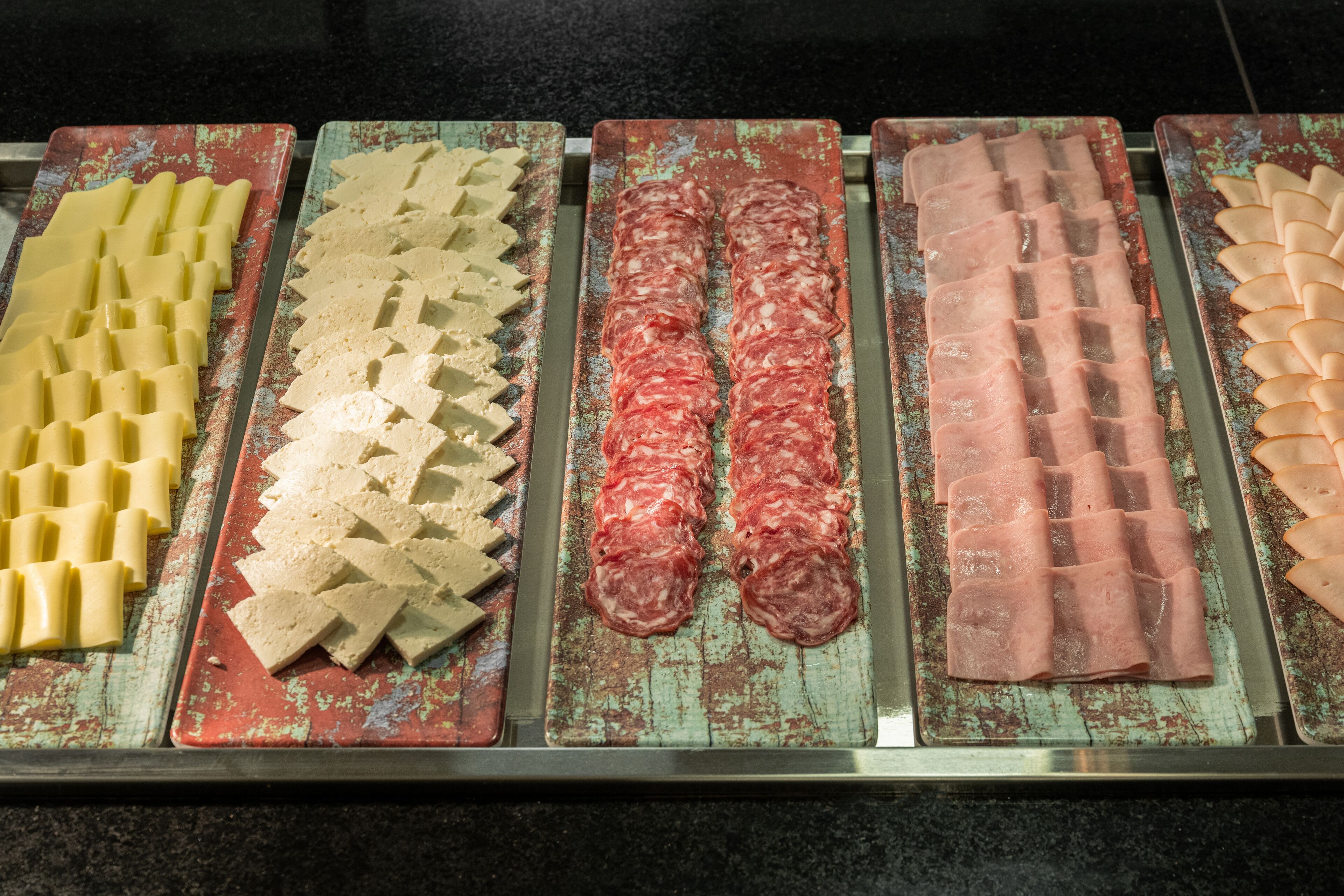 A display of various food items, including sliced meats and cheeses, arranged on metal trays.