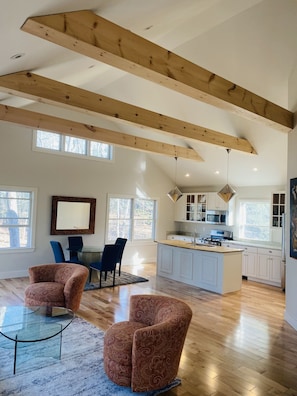 A spacious living area with a wooden ceiling, a dining table with chairs, a kitchen with white cabinets, and a large window. - Reset and Relax in Luxury Cottage (Rhinebeck)