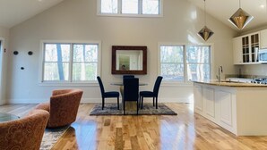 A spacious living room with a high ceiling, wooden beams, a dining area with a table and chairs, and a kitchen with white cabinets. - Reset and Relax in Luxury Cottage (Rhinebeck)
