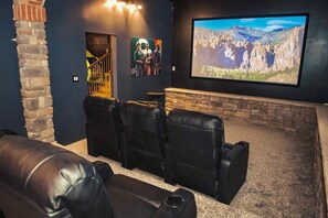 A home theater with black leather recliners, a stone fireplace, and a large screen displaying a mountainous landscape. - Pickleball, theater, game room, hot tub, & gym! (Stroudsburg)