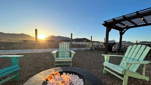 Una chimenea con piedras, dos sillas Adirondack verdes y una pérgola con luces.