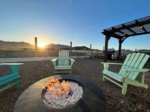A fire pit with rocks, two green Adirondack chairs, and a pergola with lights. - Mt View Villa Kingbed Firepit (Flagstaff)