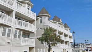 A row of multi-story buildings with balconies, a tree in the foreground, and a clear blue sky.