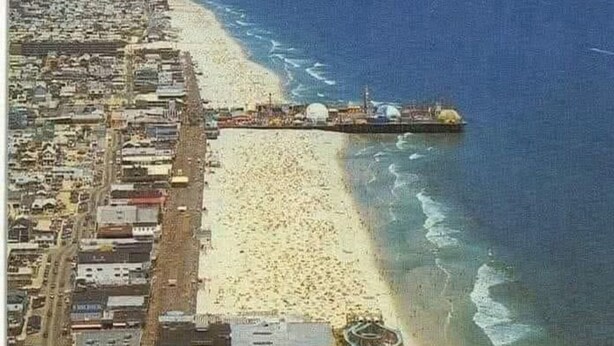An aerial view of a coastal city with a beach, a pier, and a roller coaster.